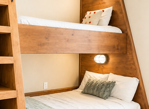 Close-up of a custom wood A-frame bunk bed with white and terracotta pillows and a sage green throw