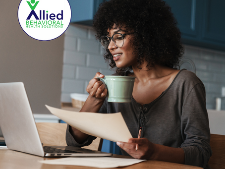 A young Black woman sits at a kitchen table, holding a mug and smiling at her laptop. She appears focused and calm, representing someone researching or considering ADHD treatment options.