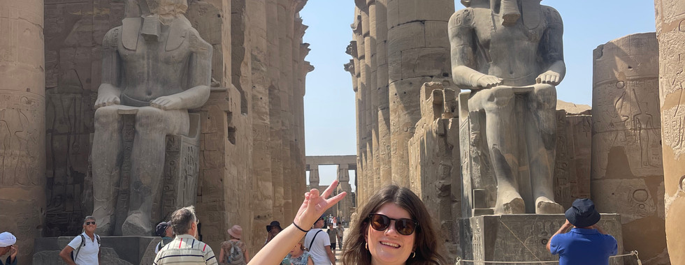 A woman holds up a piece sign in front of a statue of Ramses II in the Temple of Luxor