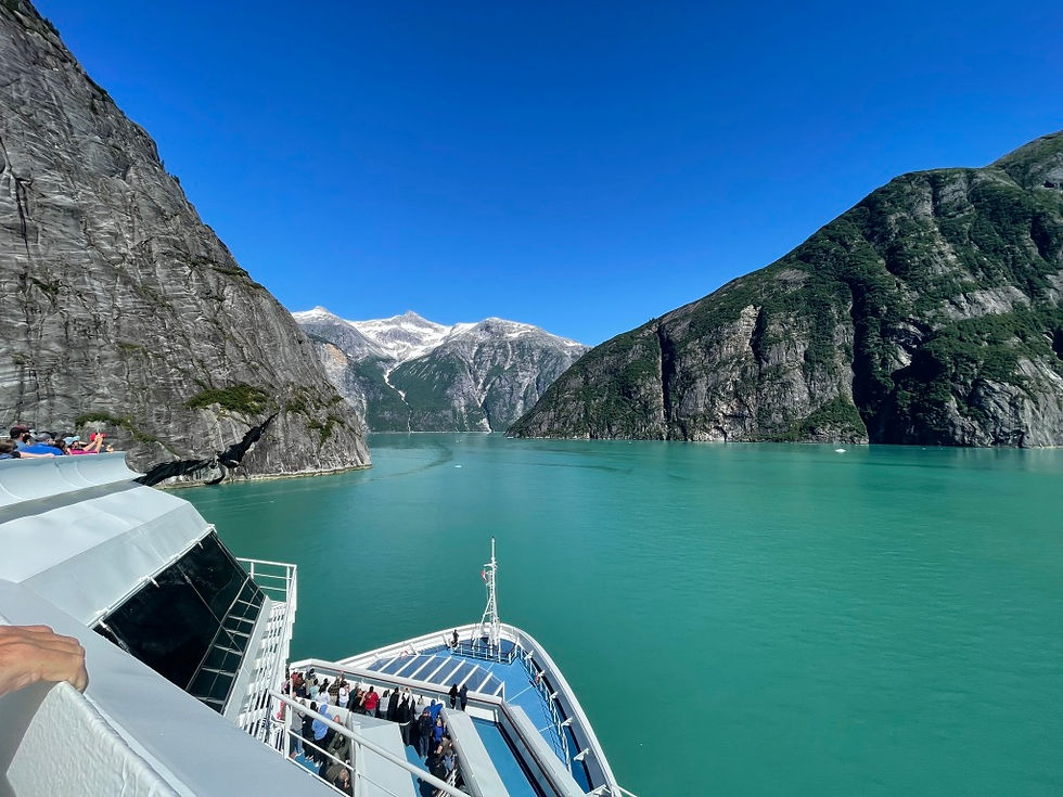 The bow of a ship entering a channel of icy blue water with mountains all around