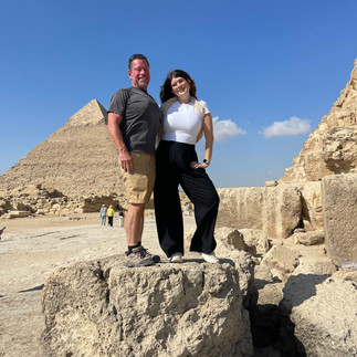 A man and woman stand on a rock with a pyramid in the distance