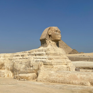 The Great Sphinx sits in the desert with a pyramid behind it