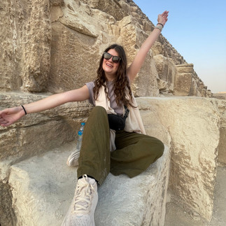 A woman sits on the wall of a pyramid with her hands in the air