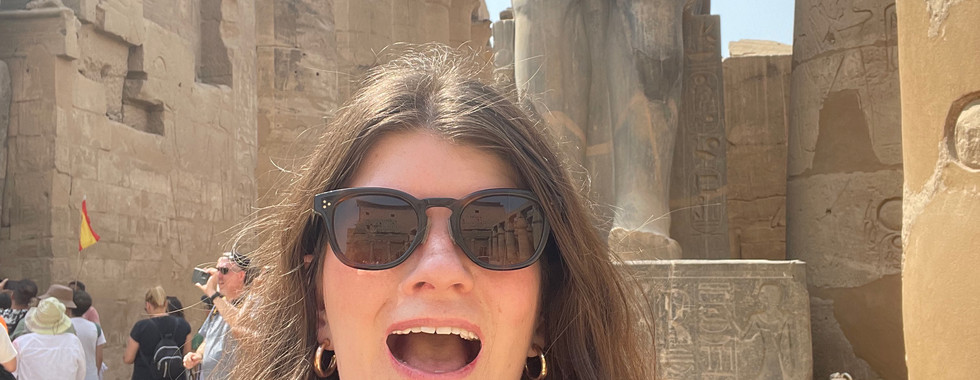 A woman smiles with a statue of Ramses II in the Temple of Luxor behind her