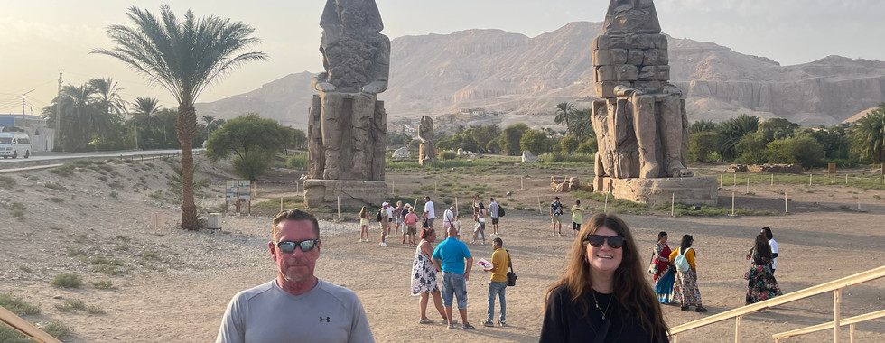 A man and a woman sit in front of the Colossi Of Memnon