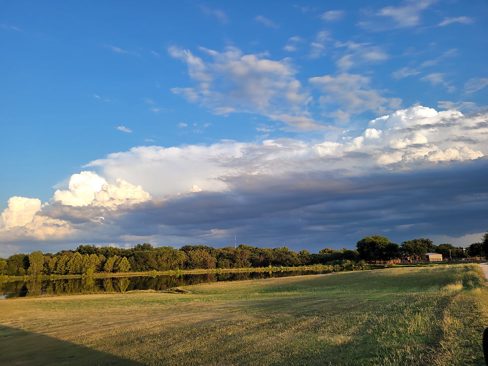 Texas field overlooking a pond with blue sky and clouds that qualifies for agricultural valuation through honey bee hive management programs.