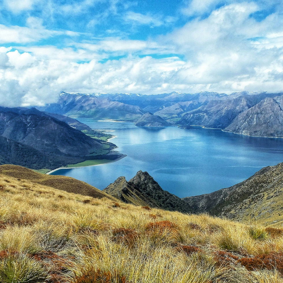 Vast blue lake in New Zealand surrounded by majestic mountains under a cloudy sky.