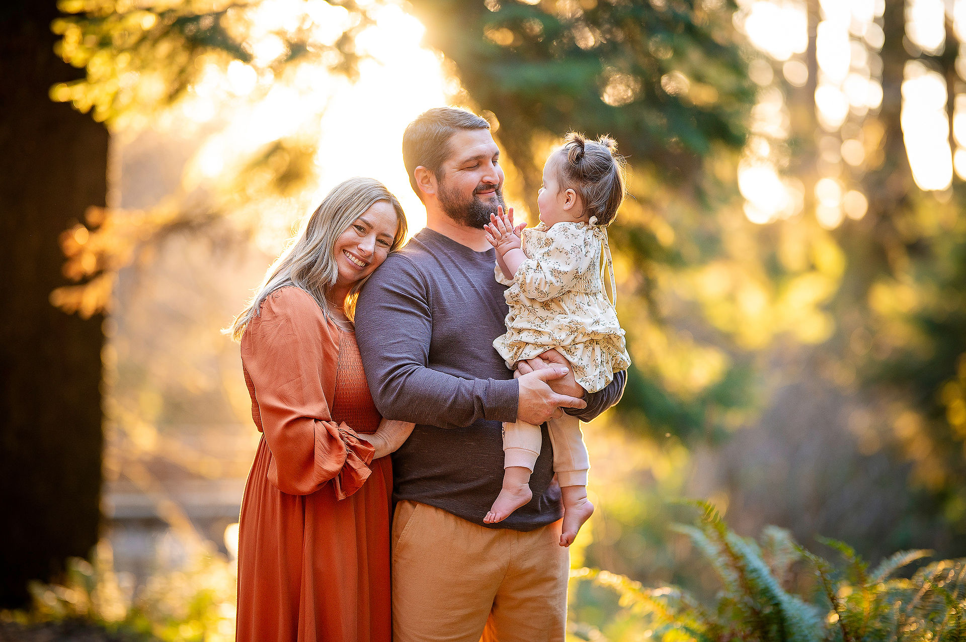 Parents holding their toddler daughter together during a golden hour family photo session on the Oregon Coast