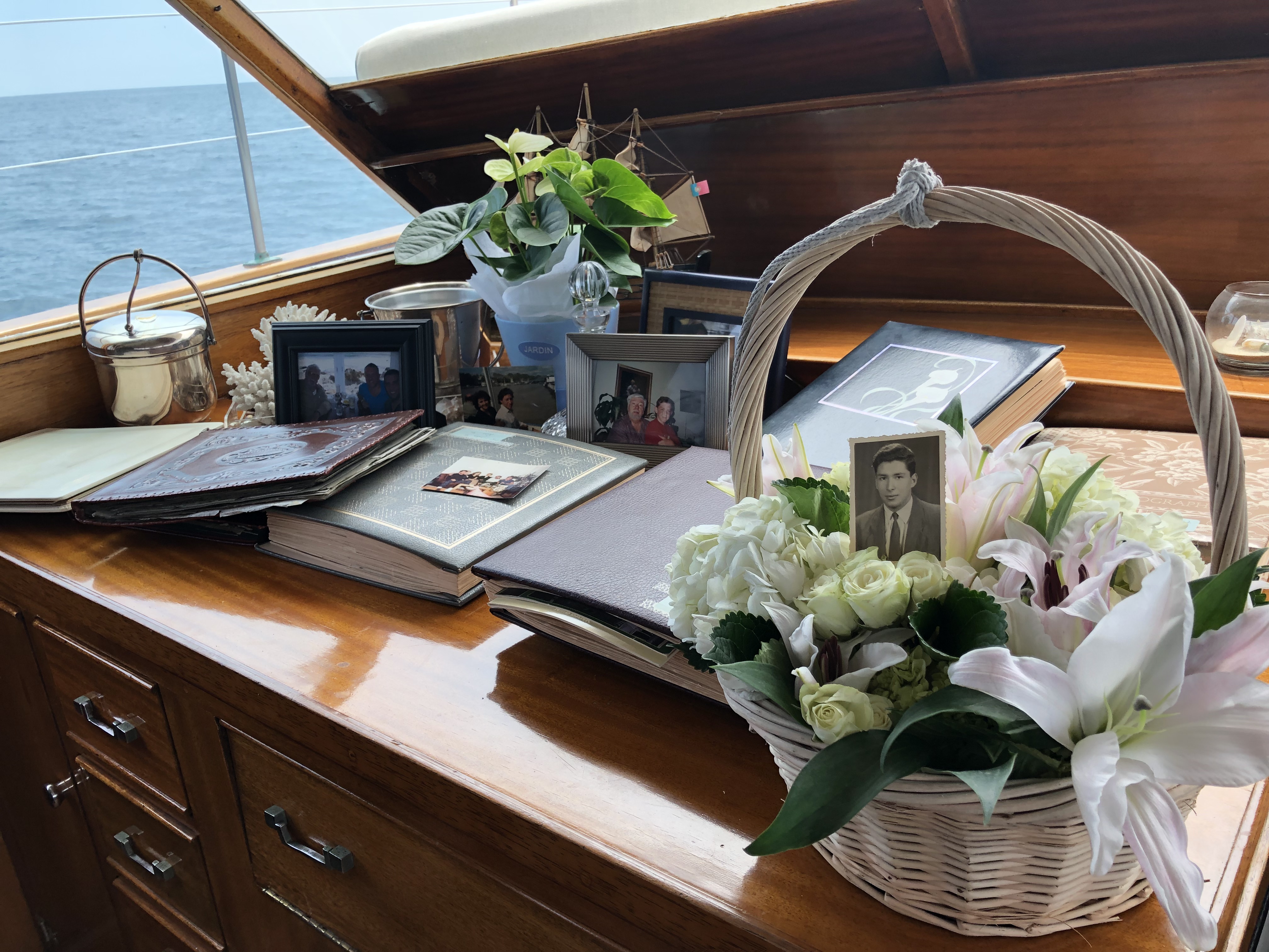 A memorial table aboard the Legend with framed photographs, photo albums, and a white floral basket, items included with every Dignified Burials at Sea ceremony