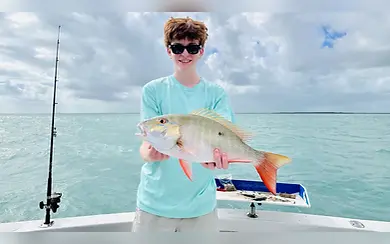 Young angler holding a snapper aboard Miss Chief with turquoise Key Largo water behind him.