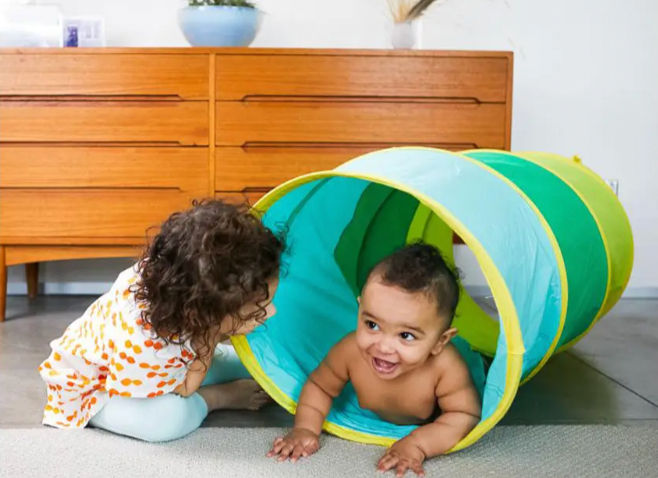 two toddlers playing together inside a crawl tunnel while practicing movement, turn-taking, and social interaction