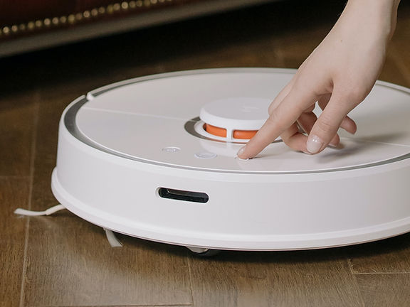 Robot süpürgeyi çalıştırma için çalıştırma düğmesine basan kadın
