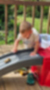 Toddler playing with toy cars on a slide outdoors