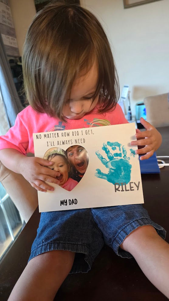 Young child holding artwork with handprint and photo