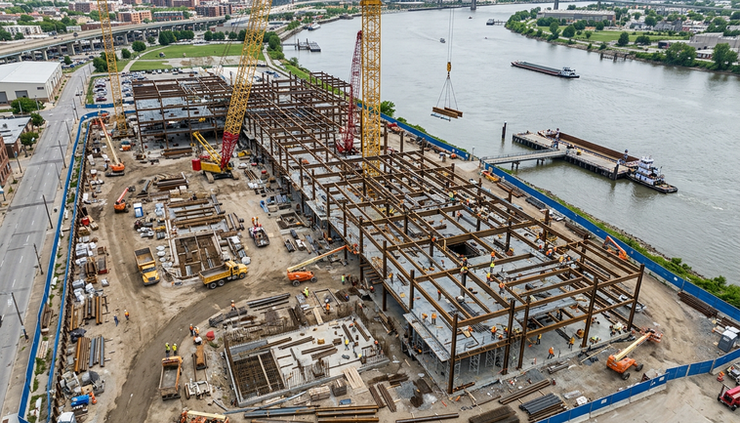 High-angle view of a construction site near a river with cranes and steel beams.
