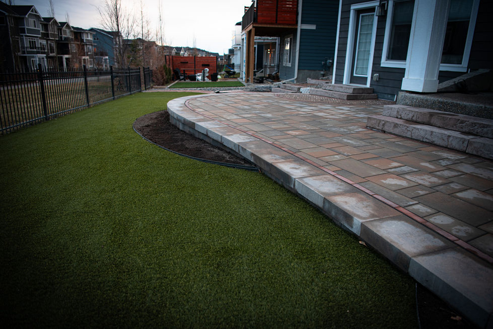 Backyard patio with large stone pavers and artificial turf edge in residential landscaping project