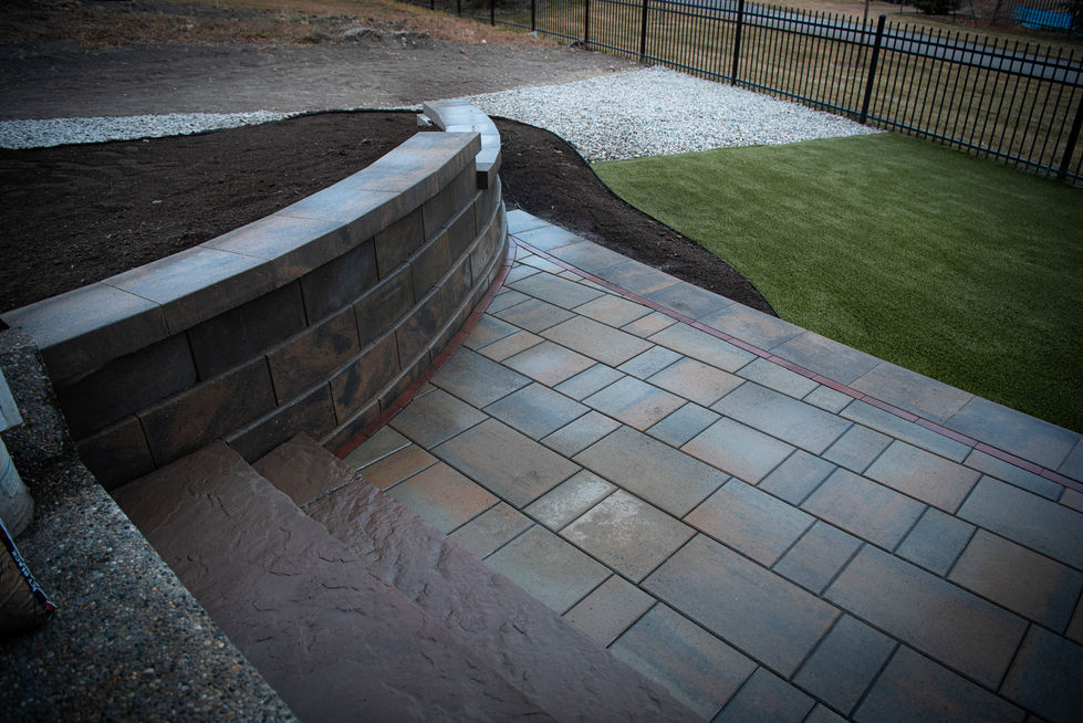 Stone patio with retaining wall and artificial turf border in Cochrane Alberta landscape design