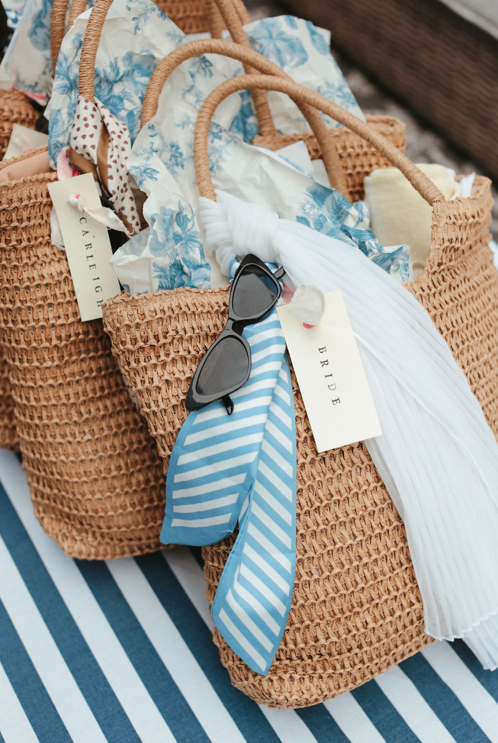 A row of straw beach bag bridesmaid gifts with sunglasses, hair scarves, organic face tallow, vintage tirrue paper