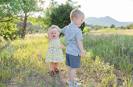 Siblings play together in a green field with Colorado Springs mountains behind them