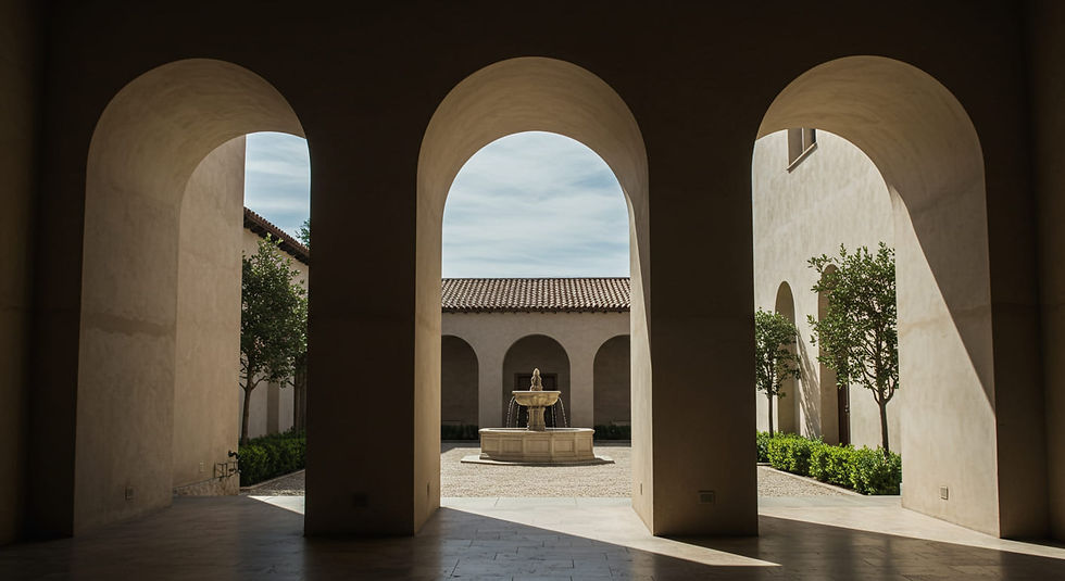 A covered loggia with smooth stucco arches overlooking a sunlit courtyard in a California Mediterranean home.