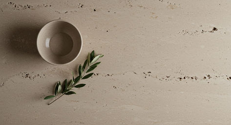 Artful top-down detail shot of a honed travertine kitchen island with a ceramic bowl and olive branch.