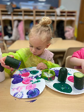 A toddler painting in a preschool classroom.