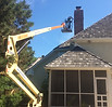 Technician performing chimney masonry repair from professional roof lift