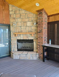 Custom-built outdoor corner fireplace with stone veneer, raised hearth, gas insert, and wood mantle on a covered porch—installed by Lakeside Chimney.