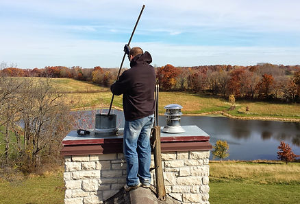Professional chimney sweeping from the roof using specialized brushes to safely remove creosote buildup.