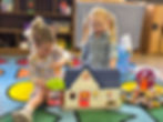 2 girls play together and share a toy doll house.