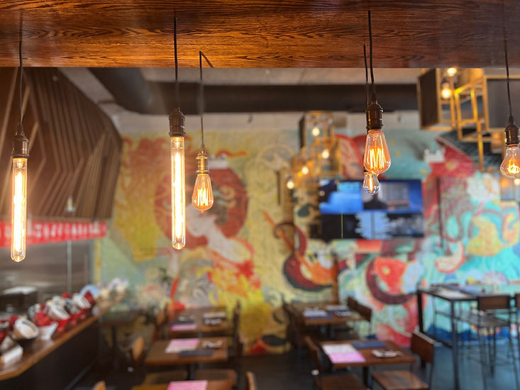 Tanaka Ramen & Izakaya interior: Edison bulb lights above dining tables and mural