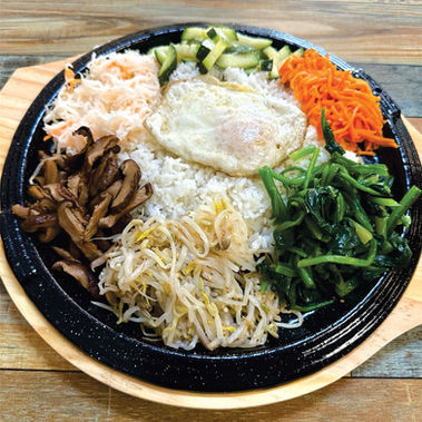 Korean bibimbap with fried egg, vegetables, and rice on a black plate. Mandoo Rang