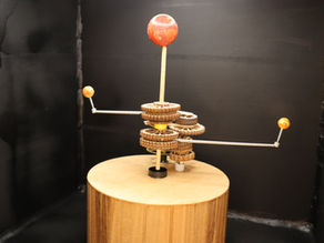 Wooden orrery depicting a sci-fi planetary system with one star and two planes. The orrery sits against a black background.