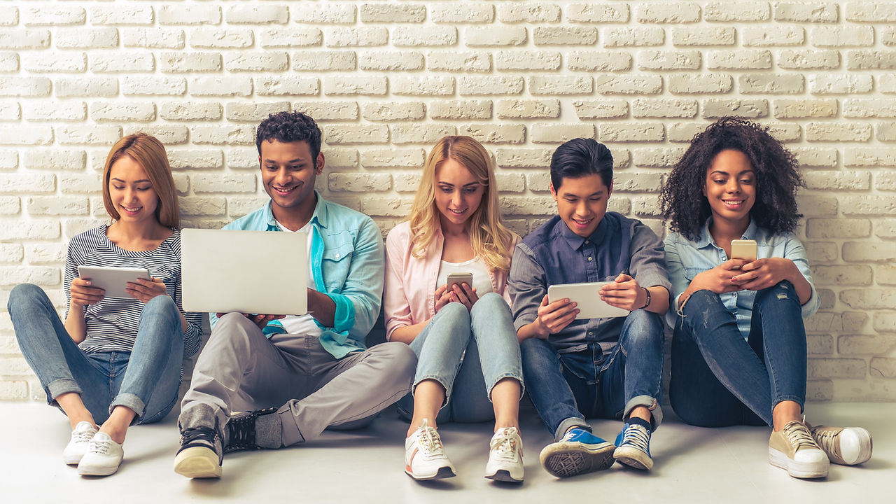 Beautiful young people of different nationalities are using gadgets and smiling, sitting against whi