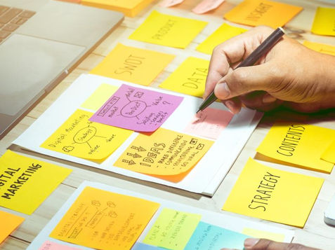 Hands writing marketing tasks on colourful sticky notes during campaign planning session.