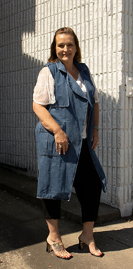 Raquel posed against a white brick wall. She is wearing a denim