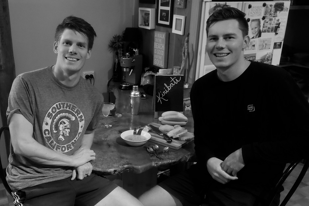 A black and white image of Aaron and his brother, Dan, sharing a meal from Kiribati together.