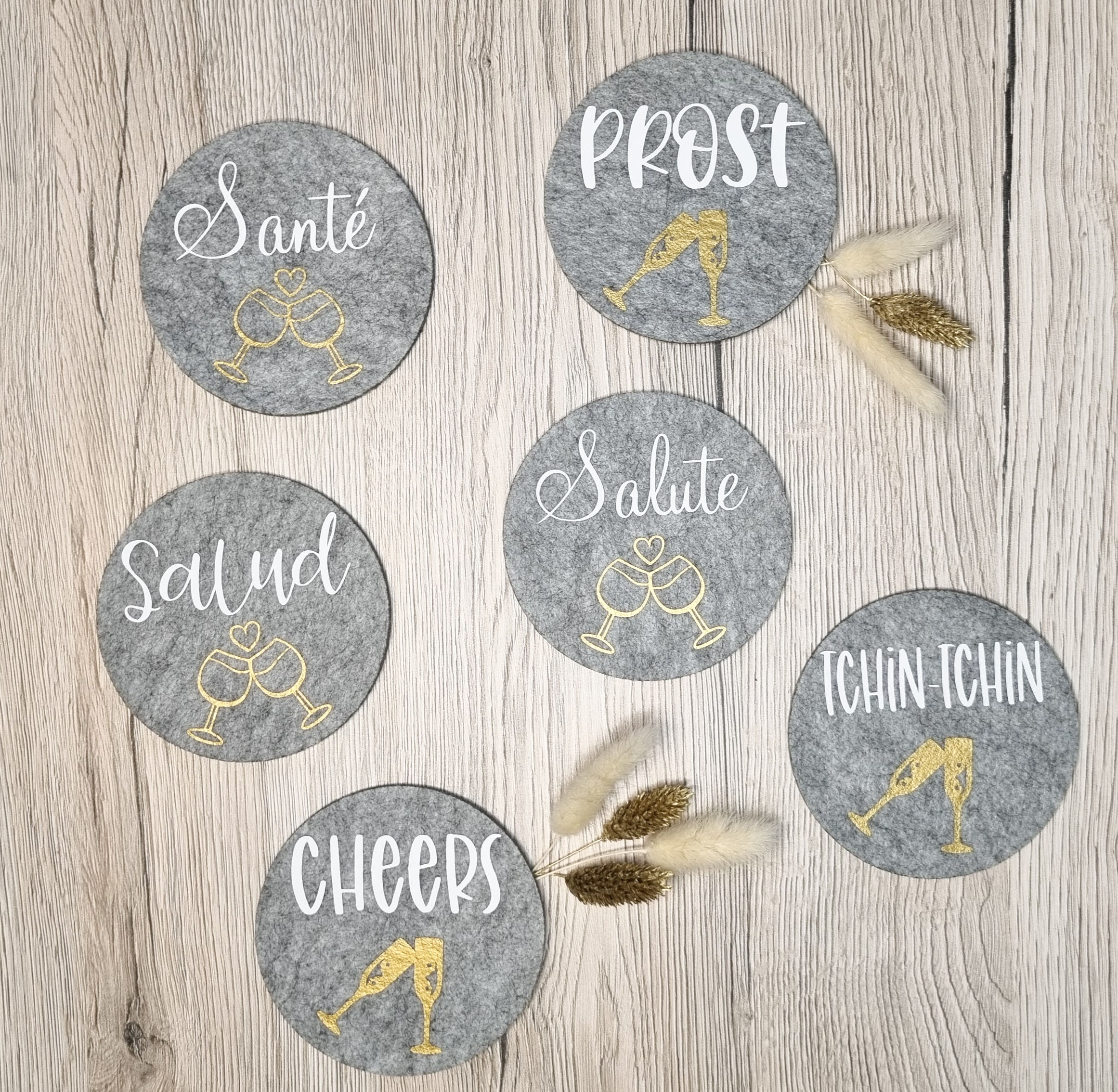 Gravierte Untersetzer mit den Worten Saluti, Prost und Cheers aus Holz auf Tisch