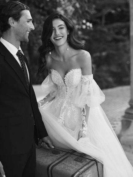 Arika Adriana Alier - A-Linien-Brautkleid aus weichem Tüll und glitzernder Blätterspitze mit tiefem Herzausschnitt, mit Carmen-trägern und einer Korsett-Schnürung. Wahlweise auch mit abnehmbaren Ärmeln erhältlich. Ideal für eine romantische Hochzeit.