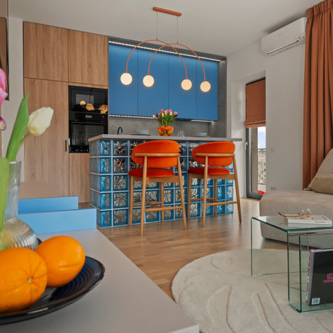 Amenajare open space proiect Cinnamon Blue: insulă de bucătărie din cărămidă de sticlă albastră iluminată și scaune de bar catifea cinnamon, într-un decor modern semnat DAS Kreative Studio.