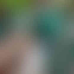 A father and a toddler are interacting on a playground climbing structure. The child is holding a large black toy steering wheel while the father leans down and smiles at her.