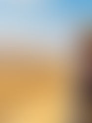 Man standing next to an off-road vehicle in a desert landscape, wearing a hat and colorful scarf, looking toward sand dunes under a blue sky.