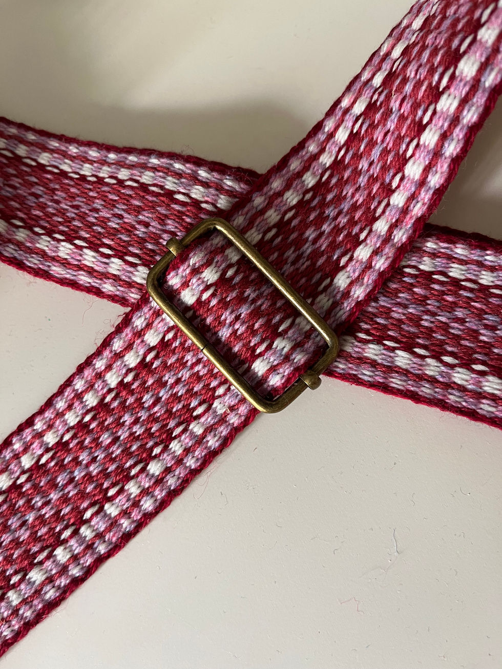 Red and pink shades of thread in a handwoven strap with metal slider