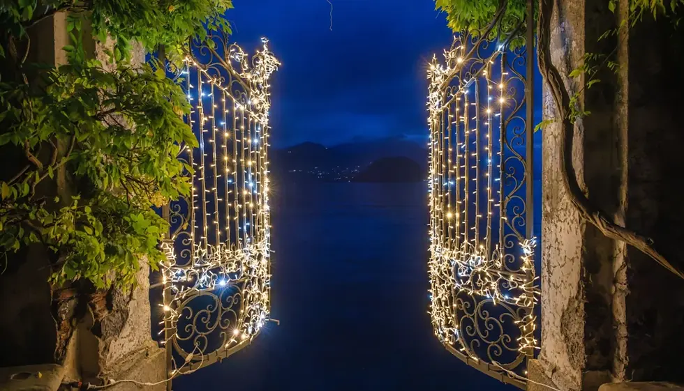 Illuminated wrought-iron gates decorated with Christmas lights opening onto Lake Como