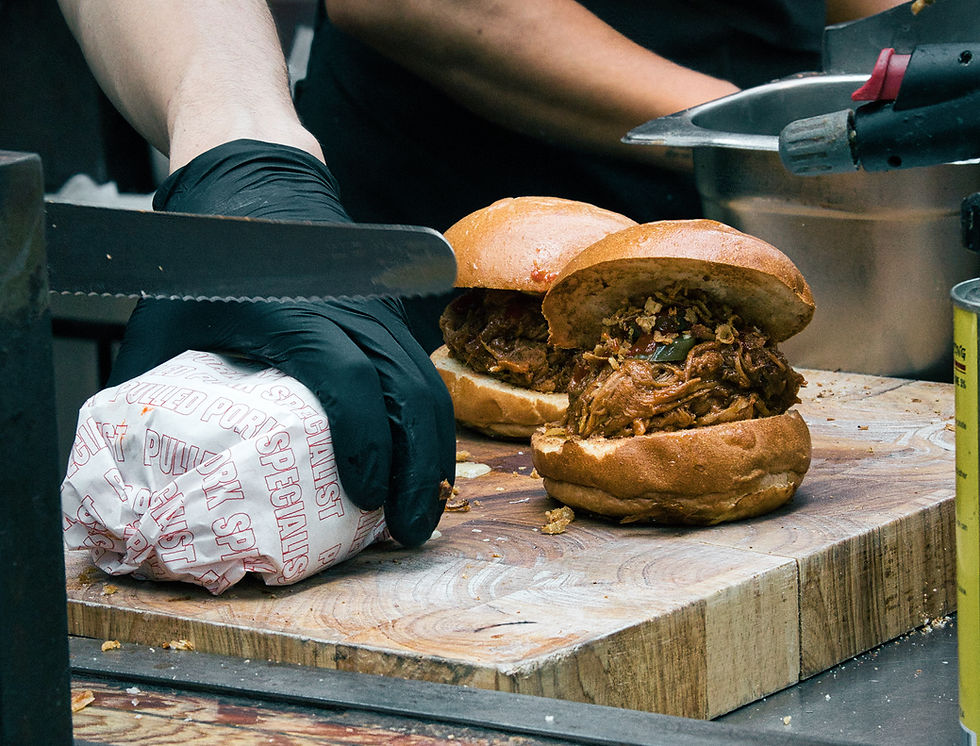 Gloved hand cuts wrapped sandwich labeled "Pulled Pork Special" beside two open pulled pork sandwiches on a wooden board.