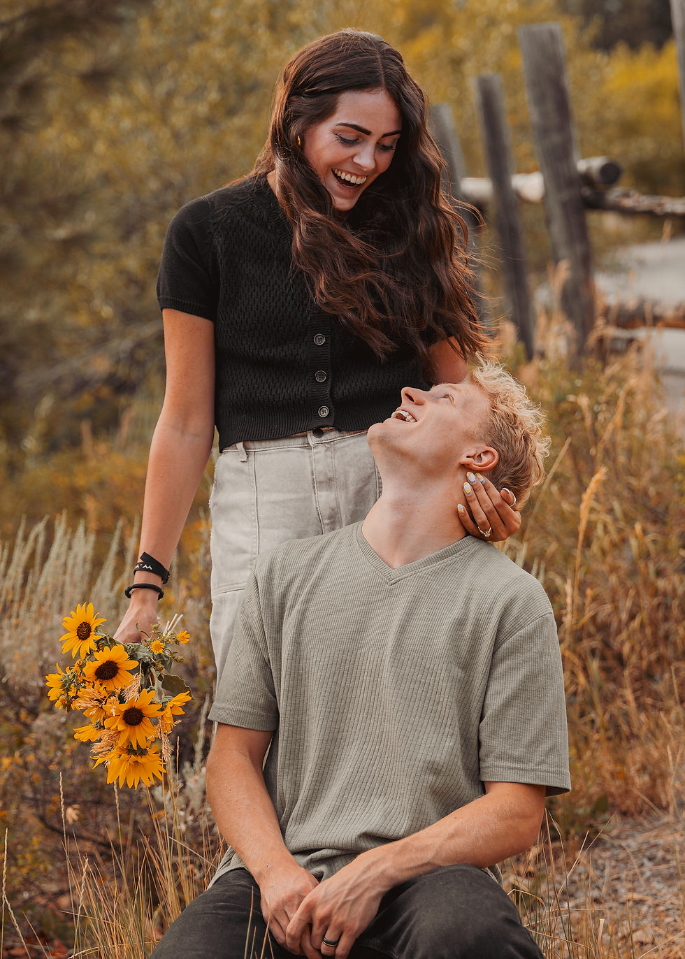 Couple sharing a joyful autumn moment, woman holding sunflowers, man looking up smiling, golden fall background.