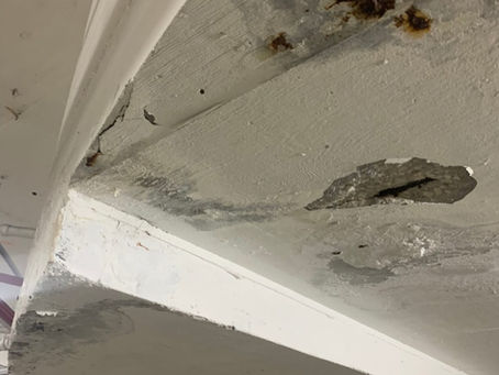 Concrete spalling and rust damage on the underside of a parking garage slab, showing signs of structural deterioration.