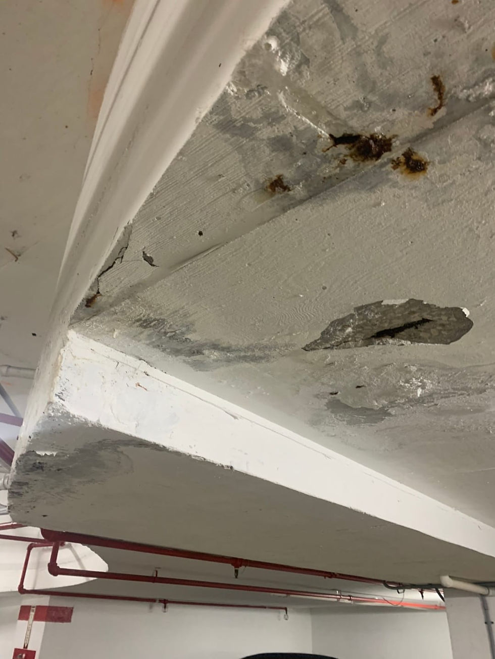 Concrete spalling and rust damage on the underside of a parking garage slab, showing signs of structural deterioration.