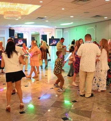 People dancing at a party, with colorful lights and Hawaiian shirts. event dj services