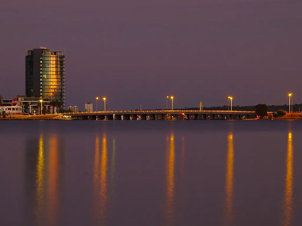 City skyline at dusk with a building, bridge, and water reflections
